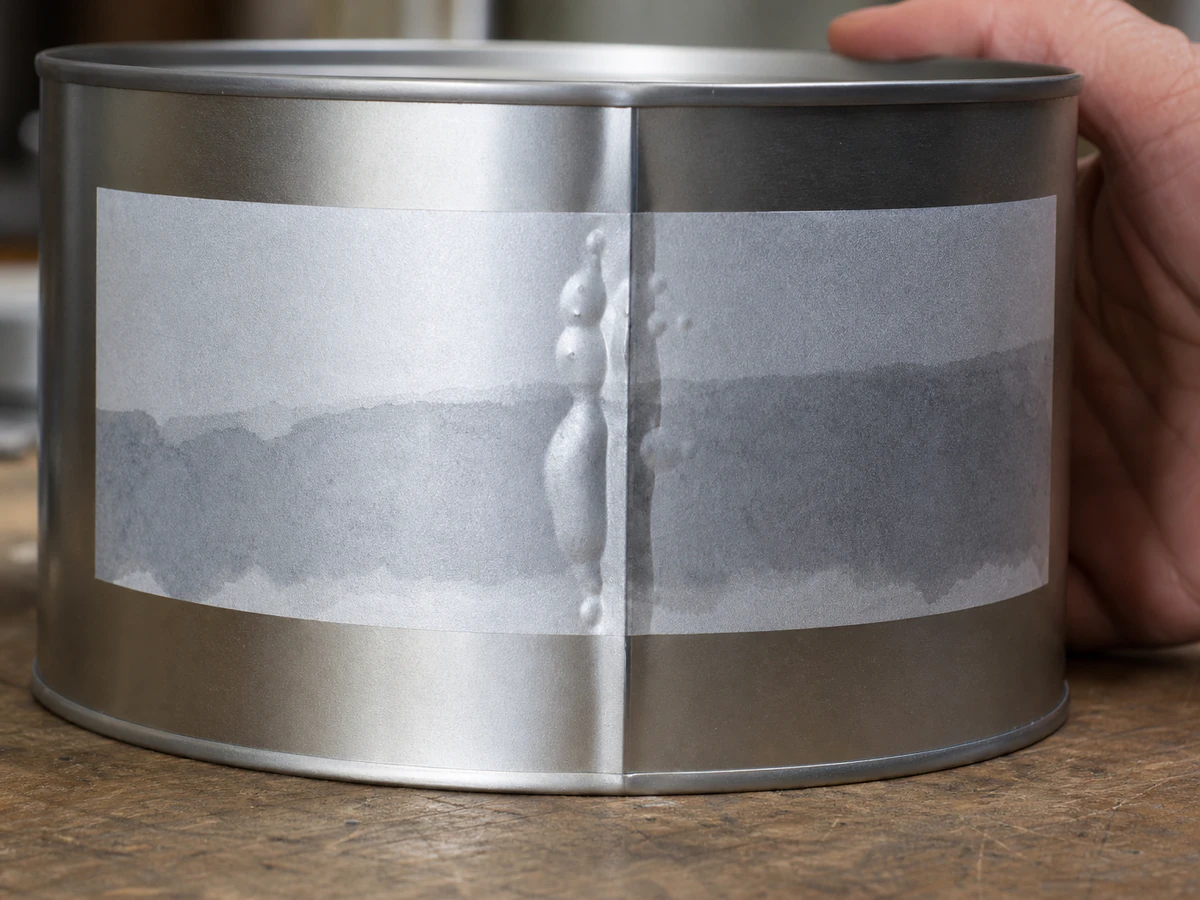 A freshly applied label on a metal tin showing trapped bubbles and a lifting corner