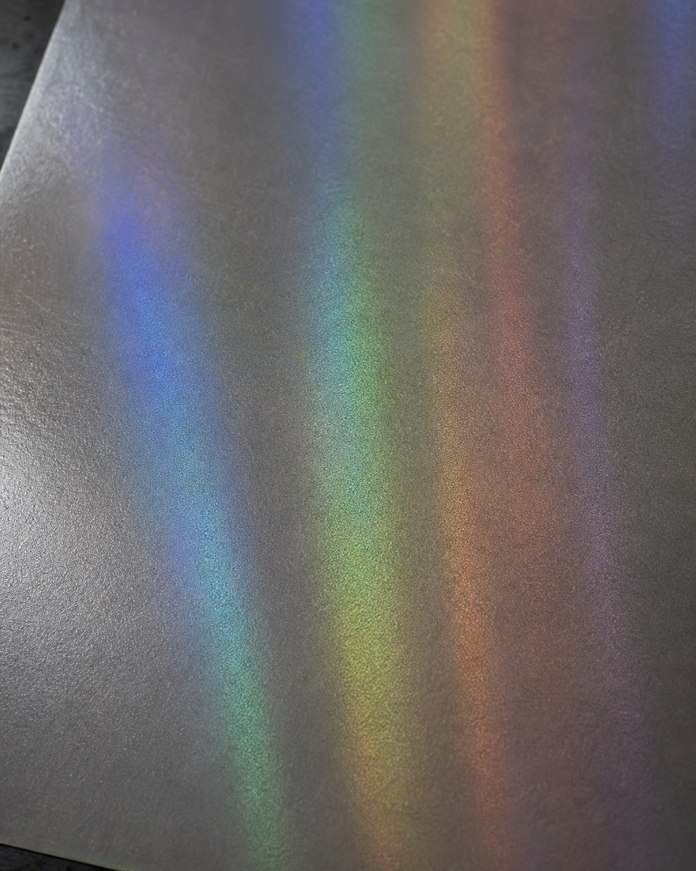 Holographic face material under raking light, its diffraction banding and surface texture filling the frame