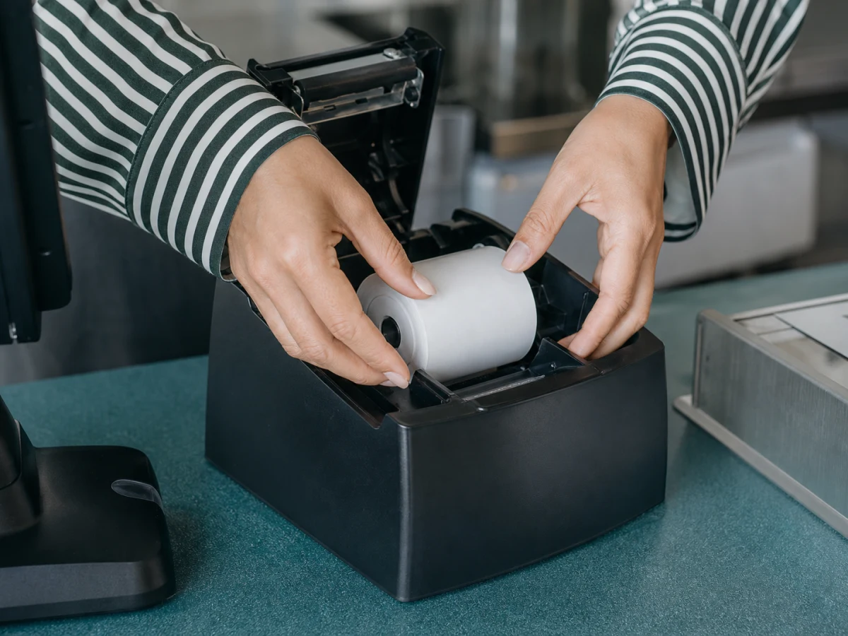 Hands loading a fresh roll into an open printer well at a counter